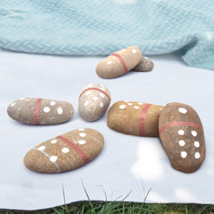 Mehrere Kieselsteine, die als Domino-Steine bemalt sind, liegend auf einer Picknick-Decke